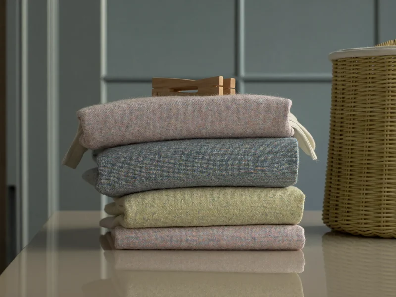 Textile pliate în nuanțe pastel, cu un coș din răchită pe masa de rufe
